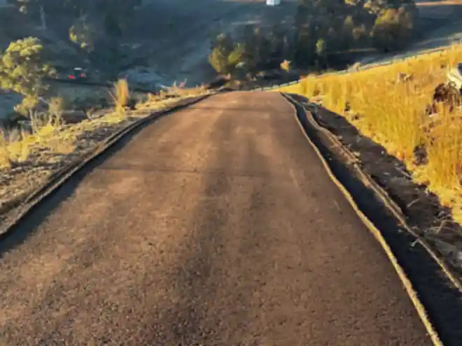 Freshly sealed rural road running over a hillside at sunrise
